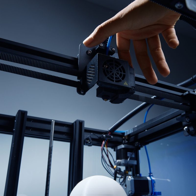 A gender-neutral hand modifying settings in 3d printer, to finish printing round white object from recycled plastic. Futuristic concept of new working possibilities for small businesses by 3D printing